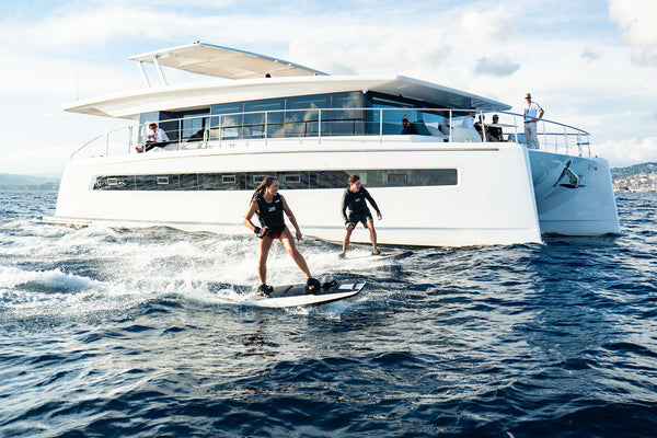 Awake electric surfboard riding in front of a yacht.