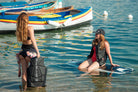 Two woman in shallow water. One is wearing the Awake Life Vest and sitting on a Jetboard. The other is holding the Awake Life Vest.